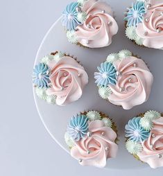 cupcakes with pink and blue frosting are arranged on a white platter