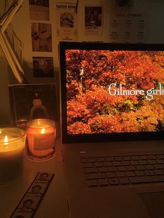 an open laptop computer sitting on top of a desk next to a candle and pictures