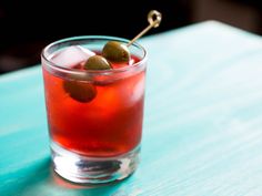 a close up of a drink on a table with an olive garnish in it