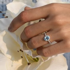 a woman's hand with a ring on it and a flower in the background