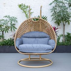 a wicker swing chair with blue cushions on a deck next to potted plants