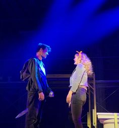 two people standing on stage with one holding a knife and the other looking at something