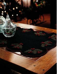 a wooden table topped with two place mats and a glass vase filled with flowers next to a christmas tree