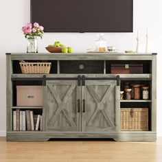 an entertainment center with sliding doors and baskets on the bottom shelf, in front of a flat screen tv