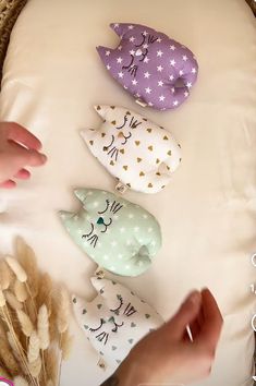 four different colored fish shaped ornaments on a white surface with two hands reaching for one