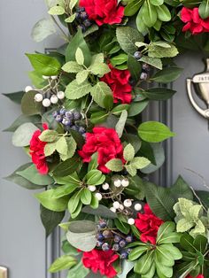 a wreath with red flowers and green leaves hanging on the front door to welcome guests