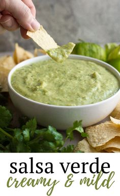 a person dipping guacamole into a bowl with tortilla chips on the side