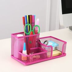 a pink desk caddy with pens, scissors and other office supplies in it on a white table