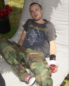 a man in camouflage pants sitting on a chair with a cup of coffee next to him