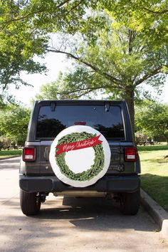 a black jeep with a wreath on it's back door is parked in front of a tree