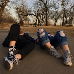 two people laying on the ground with their legs crossed and one person wearing ripped jeans