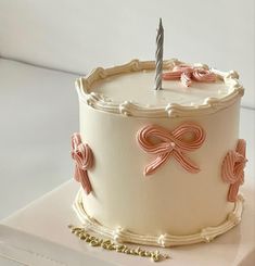 a white cake with pink bows and a single candle