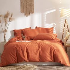 an orange bed in a white bedroom with pillows and blankets on the floor next to a lamp