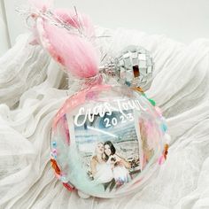 a glass ornament with a photo on it and a pink feather hanging from the top