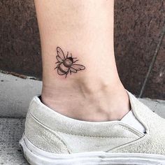 a small tattoo on the ankle of a woman's foot with a bee on it