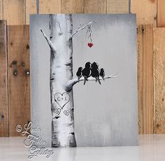 two birds sitting on a tree branch in front of a wooden fence with hearts hanging from it