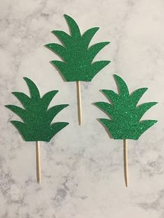 three green pineapple picks on a white marble counter top with glittery paper leaves