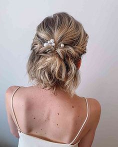 a woman with blonde hair wearing a white tank top and pearls in her hair, back view