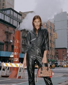 a woman standing on the street holding a leopard print purse and wearing black leather pants