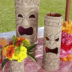 there are three vases made to look like tiki faces and flowers on the table