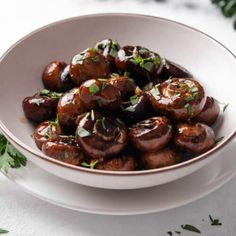 a white bowl filled with cooked mushrooms and garnished with parsley on top