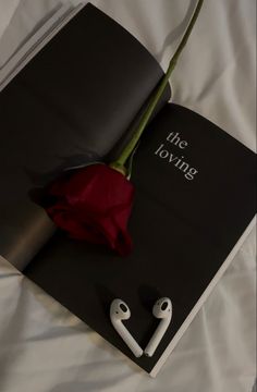 an open book with ear buds and a red rose on the cover that says, the dying