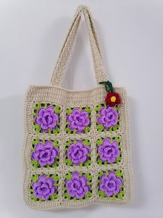 a crocheted bag with purple flowers on the front and green leaves on the back