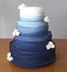 a blue and white wedding cake with flowers on the bottom tier, sitting on top of a wooden table