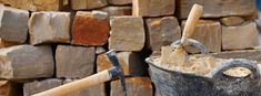 a bucket full of sand next to a pile of bricks with an ax sticking out of it