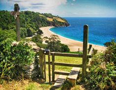 a wooden gate on the side of a hill next to an ocean and sandy beach