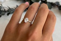 a woman's hand with a diamond ring on top of her finger and flowers in the background