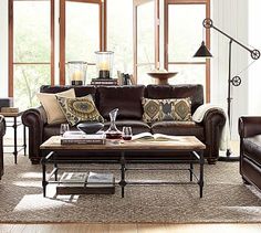 a living room filled with lots of furniture next to tall windows and floor lamps on either side of the couch