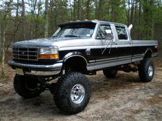 a large black truck parked on top of a dirt road in front of some trees