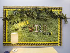 a green wall hanging on the side of a blue wall next to a table with a lamp