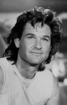 a black and white photo of a man with long curly hair wearing a tank top