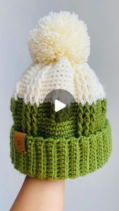 a hand holding a green and white knitted beanie with a video play button