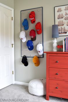 a baseball cap organizer hanging on the wall next to a red dresser and orange chest