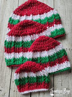 two red and green knitted hats sitting on top of a wooden table