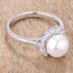 a pearl and diamond ring sitting on top of a wooden table