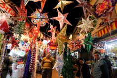 people are walking through an open market with many colorful decorations hanging from it's ceiling