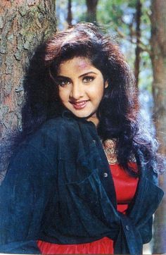 a woman standing next to a tree with long hair and wearing a red dress in the woods