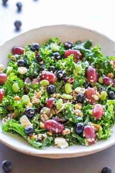 a salad with grapes, nuts and broccoli in a white bowl on a table