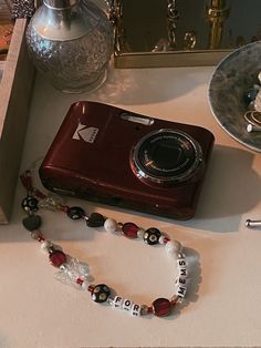 a red camera sitting on top of a table next to a white and black beaded necklace