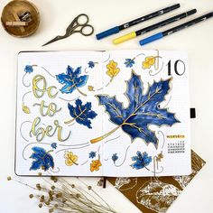 an open notebook with leaves on it next to some markers and pens, along with other art supplies