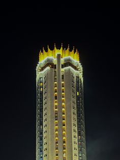 a very tall building lit up at night with lights on it's sides and the sky in the background