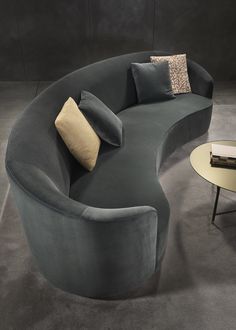 a curved couch with two pillows on top of it next to a table and chair