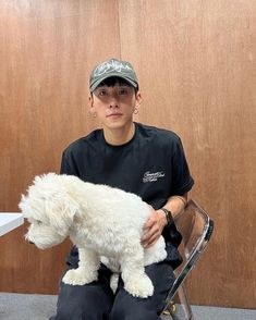 a boy sitting on a chair holding a white dog in his lap and looking at the camera