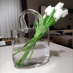 white tulips are in a clear glass vase on a counter top with water