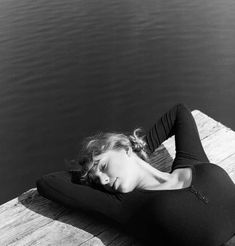 a black and white photo of a woman laying on a dock with her eyes closed