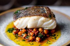 a white plate topped with fish covered in sauce and garnished with chickpeas